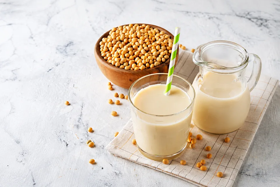 Soy beverage in a glass and pitcher beside whole soybeans
